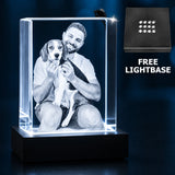 A personalized acrylic LED light box displaying a photo of a man holding a dog, shown on a black base against a dark blue background. A small inset at the top right shows a feather decoration, and text at the right reads 'FREE LIGHTBASE'.